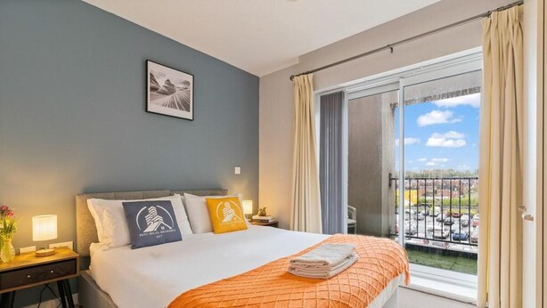 Habitación de hotel con cama, mesita de noche, lámpara, un cuadro en la pared y un balcón con vista al estacionamiento.