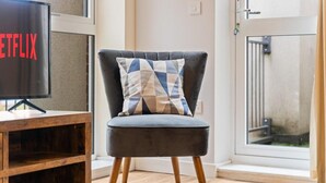 Una sala moderna con un sillón tapizado en gris, una mesita de madera y un televisor que muestra el logotipo de Netflix.