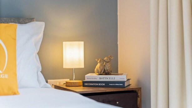 A neatly made bed with a yellow pillow, a bedside lamp, and a decoration book on a wooden nightstand. - Tranquil Telford Retreat With 2 Bedrooms (Telford)