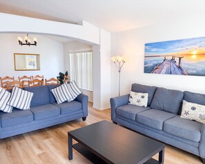 A living room with two grey sofas, a black coffee table, a wooden dining table with chairs, a floor lamp, a painting of a sunset, and a mirror on the wall. - WS118LD - Lakeview paradise 4 Bedrooms Pool Villa (Davenport)