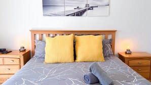 A bed with a grey and white tree branch pattern bedspread, two yellow pillows, a grey towel, and a wooden headboard.