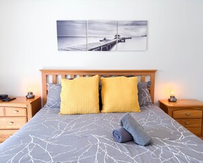 A bed with a grey and white tree branch pattern bedspread, two yellow pillows, a grey towel, and a wooden headboard.