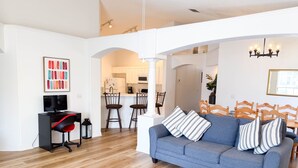 A living room with a sofa, a coffee table, a TV, and a kitchen in the background.