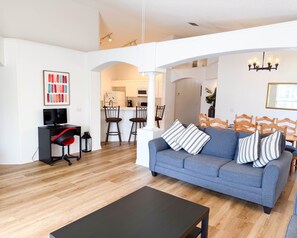 A living room with a sofa, a coffee table, a TV, and a kitchen in the background.