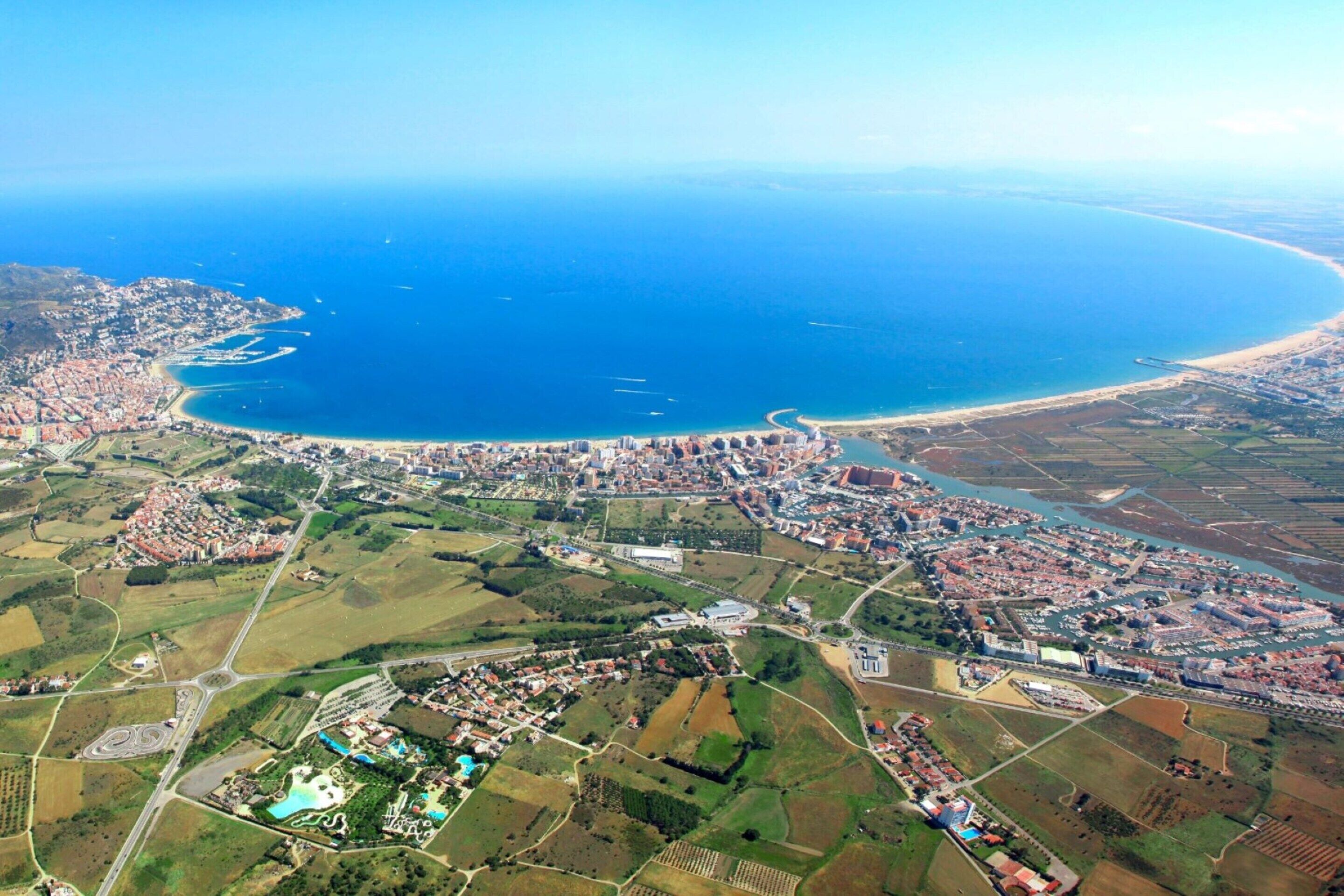 Eine Vogelperspektive einer Küstenstadt mit Strand, Wohngebieten und landwirtschaftlichen Feldern.