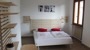 A modern bedroom with a bed, red pillows, a wooden headboard, and artwork on the wall. - All'Antico Ulivo (Artegna)