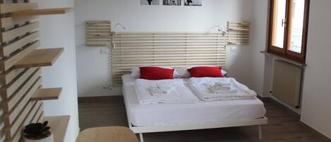 A modern bedroom with a bed, red pillows, a wooden headboard, and artwork on the wall.