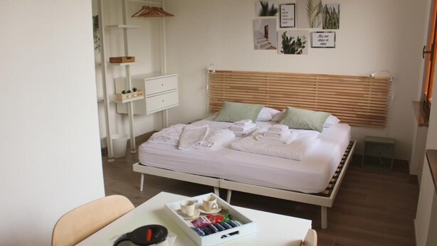 A neatly arranged bedroom with a bed, bedside table with towels, a small table with a tray of toiletries, and a wall with framed pictures. - All'Antico Ulivo (Artegna)
