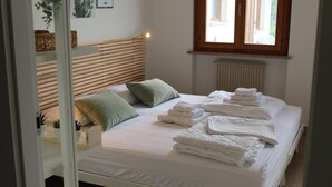 A neatly made bed with folded towels, a wooden headboard, and a window with blinds. - All'Antico Ulivo (Artegna)