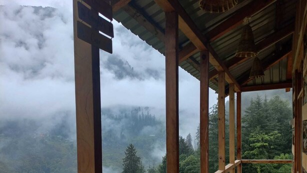A wooden deck with a bench overlooking a forested valley shrouded in mist. - Shangarh Kothi (Sainj)