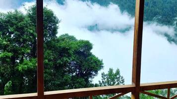 Un balcon en bois offrant une vue sur une vallée boisée et des montagnes enveloppées de brume.