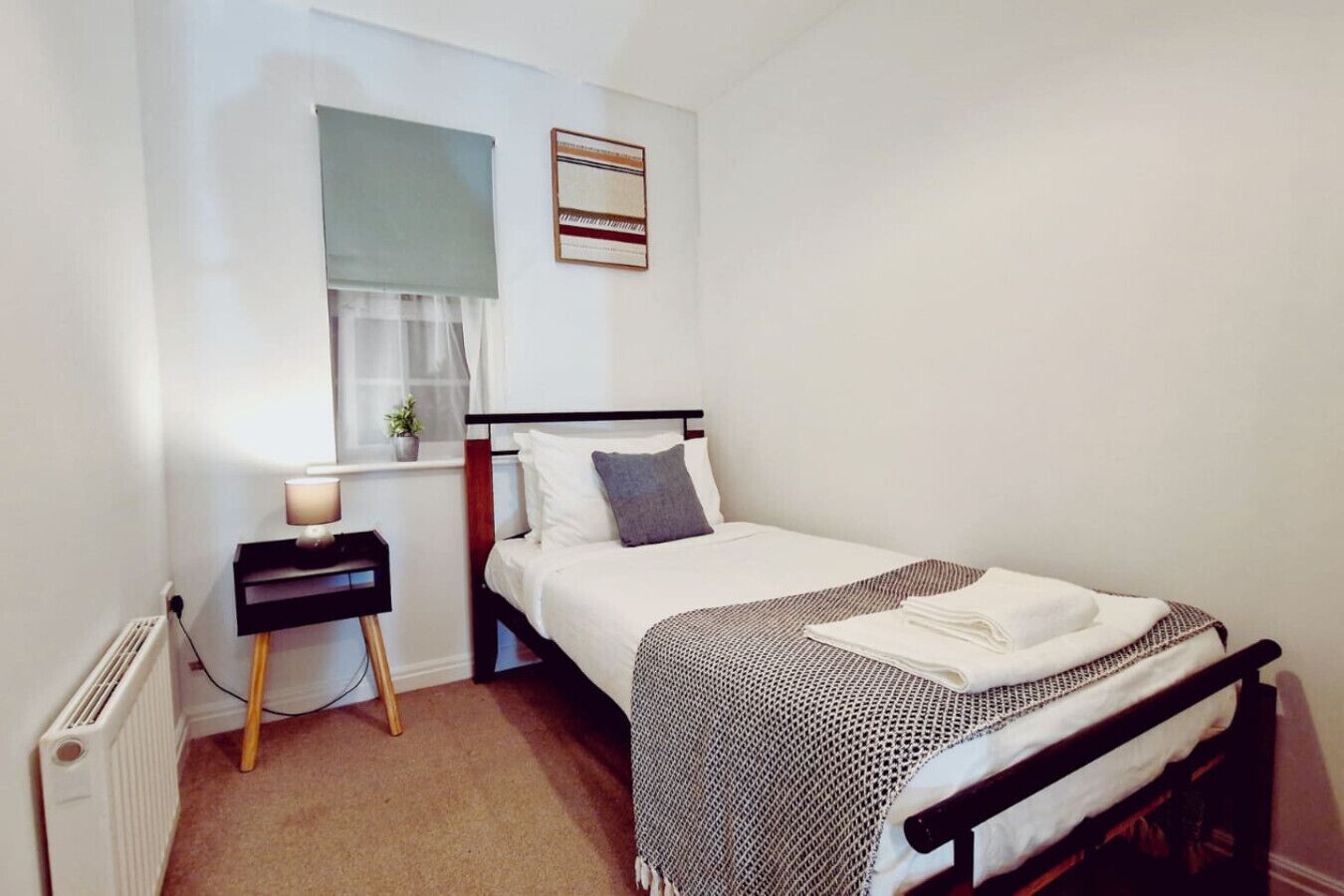 Un dormitorio con cama, mesita de noche y ventana con cortina.