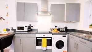 A modern kitchen with grey cabinets, a built-in oven, a microwave, a toaster, and a washing machine. - Barn Fold House with Parking, Garden, Wi-Fi (Telford and Wrekin)
