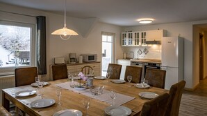 Comedor con mesa de madera dispuesta para seis comensales, cocina con alacenas blancas y vista a un paisaje nevado a través del ventanal.