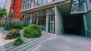 A modern building with a glass facade, a sign reading "Lobby Residencial", and a well-maintained garden area in front.