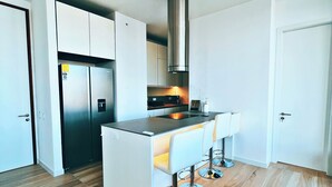 Een moderne keuken met witte kastjes, een roestvrijstalen afzuigkap en een centraal kookeiland met barstoelen.