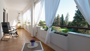 Ein Balkon mit weißem Stuhl, einem kleinen Tisch mit Topfpflanze und Blick ins Grüne.