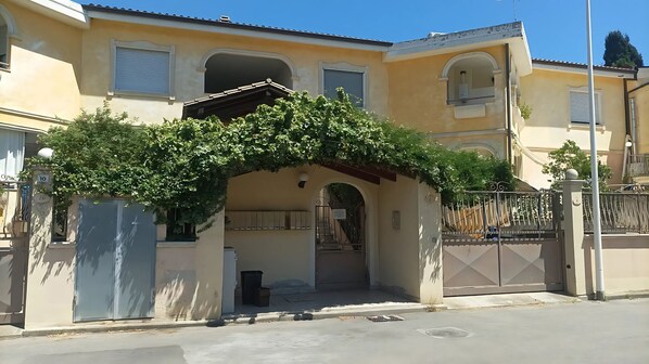Un bâtiment doté d’une entrée abritée, d’une allée bordée de portails et d’un escalier menant à un étage supérieur.