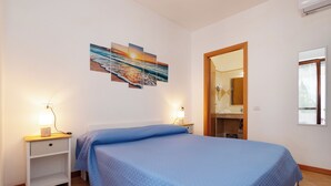 Ein Schlafzimmer mit einem Bett, zwei Nachttischen mit Lampen, einem Wandbild und einer Tür zu einem Badezimmer.