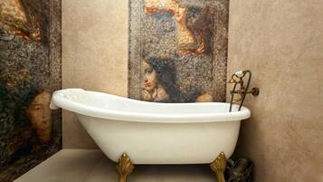 Una bañera independiente con patas ornamentales, ubicada en un baño con piso de baldosas y una pared decorativa con diseño de mosaico.