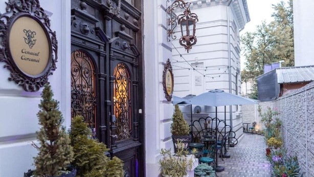 An outdoor café area with tables and chairs, potted plants, and a decorative door with a sign. - Conacul Coroanei Luxury Boutique (Bucharest)
