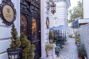 An outdoor café area with tables and chairs, potted plants, and a decorative door with a sign. - Conacul Coroanei Luxury Boutique (Bucharest)