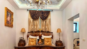 A bedroom with a large bed, ornate headboard, two bedside lamps, and a chandelier. - Conacul Coroanei Luxury Boutique (Bucharest)
