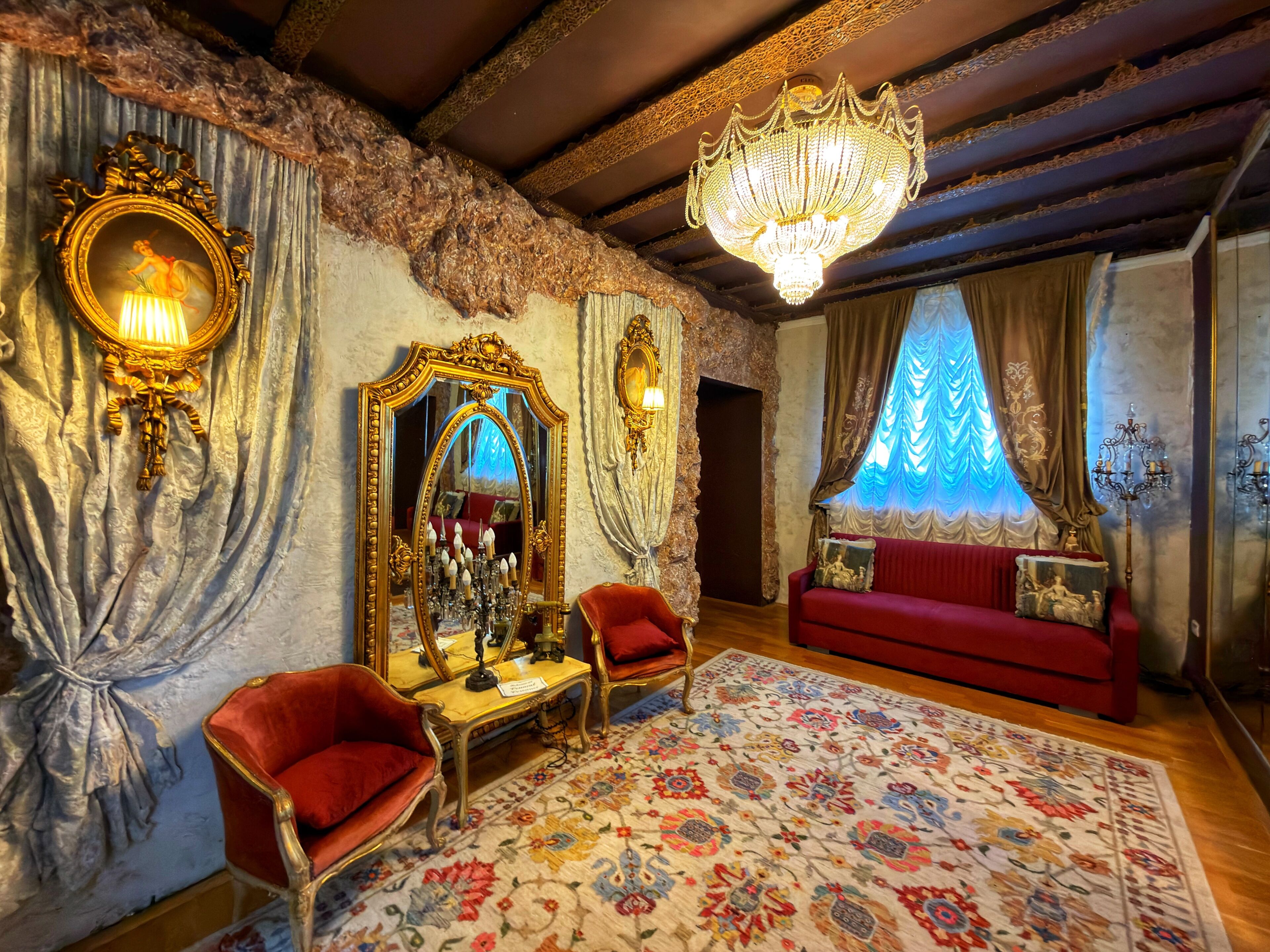Una habitación con candelabro, espejo decorativo, sofá rojo y alfombra floral.