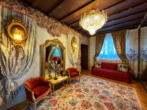Una habitación con candelabro, espejo decorativo, sofá rojo y alfombra floral.