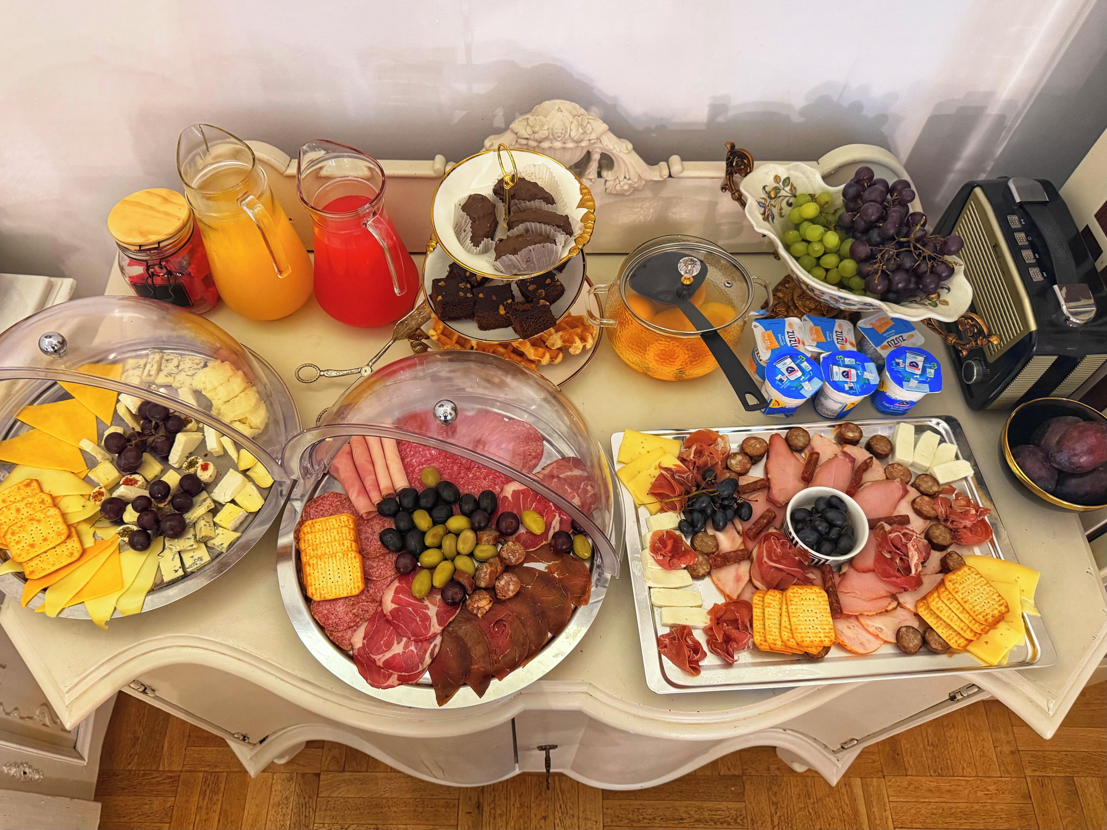 A buffet table with various food items including meats, cheeses, fruits, and beverages.