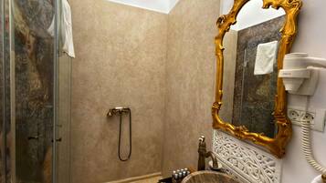 Un baño con pared de mármol, espejo con marco dorado, lavamanos con cuenca de madera y ducha de mano.