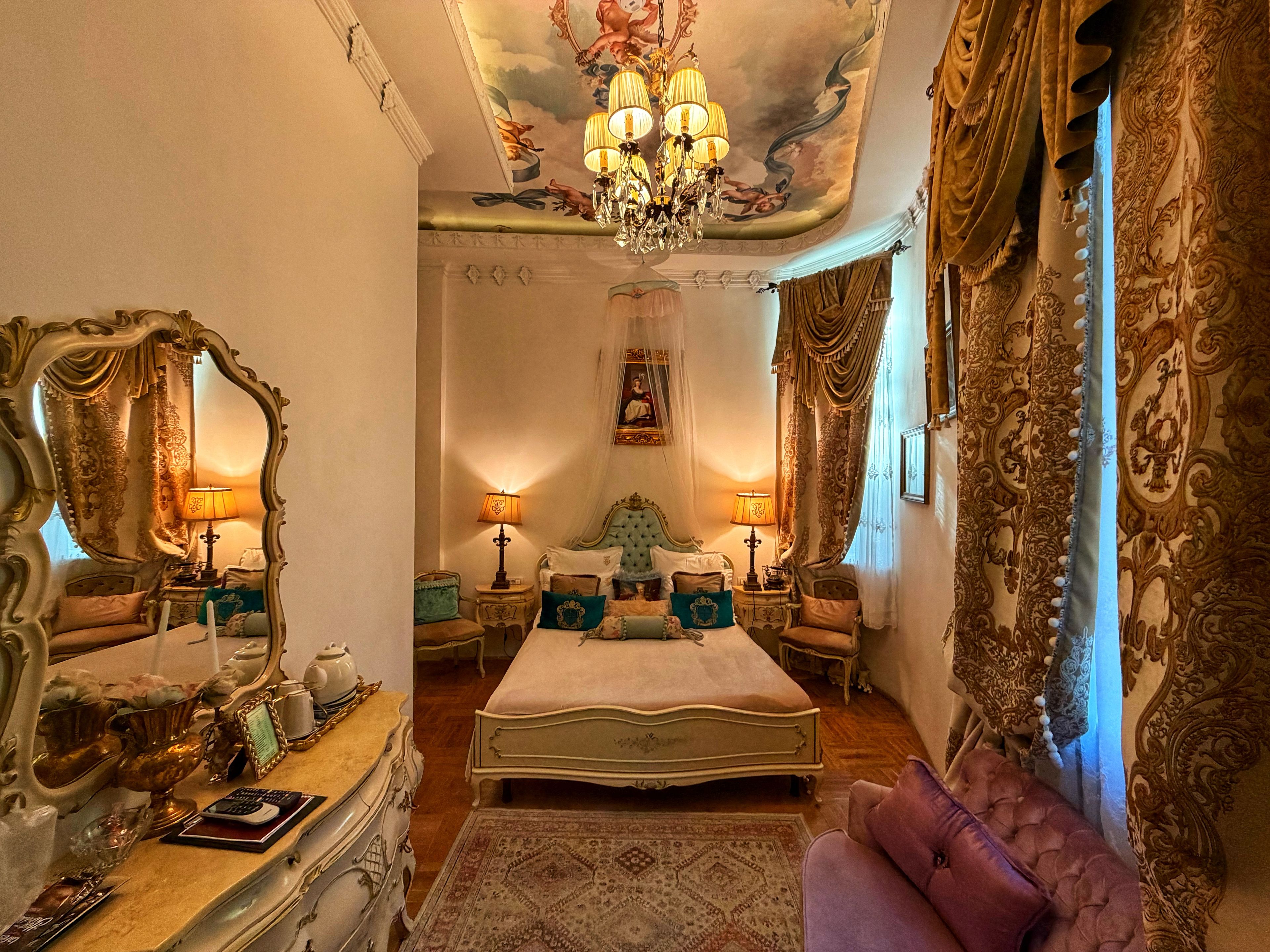 A luxurious bedroom with a large bed, ornate furniture, and a chandelier.