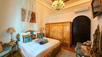 Une chambre à coucher luxueuse, dotée d’un grand lit, de meubles richement décorés et d’un lustre.