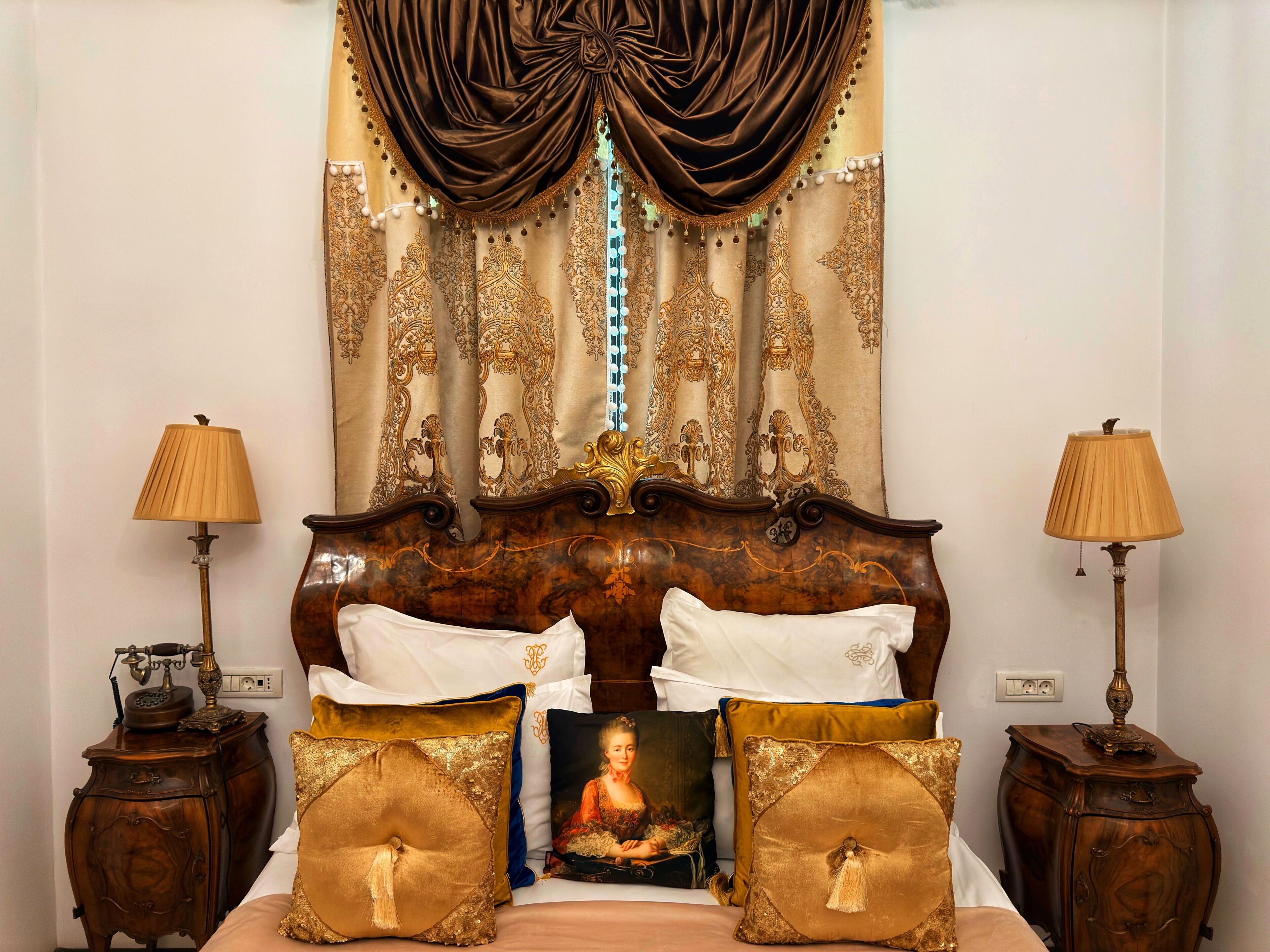 Una cama con cabecera decorada, almohadillas decorativas y un cuadro enmarcado. Hay dos mesitas de noche con lámparas.