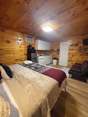 Interior acogedor de una cabaña con cama, sofá, kitchenette y puerta.