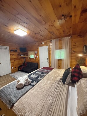 A cozy cabin room with a bed, a sofa, a television, and a fireplace. - Riverfront King Cabin,  Cozy RRG Escape for 2 (Stanton)