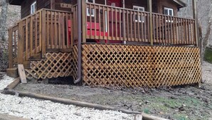 Una cabaña de madera con un porche, una puerta roja y un balcón pequeño.