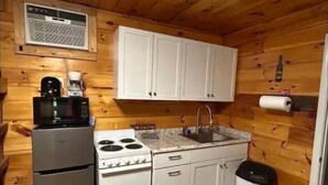 Cocina compacta con gabinetes blancos, estufa, microondas, pileta y basurero.