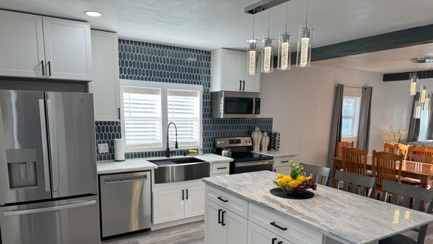 A modern kitchen with stainless steel appliances, a marble island, and a dining area with wooden chairs.
