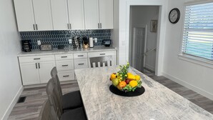A modern kitchen with white cabinets, a marble countertop, and a fruit bowl.