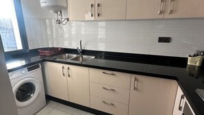 Une cuisine moderne avec des meubles de couleur beige, un plan de travail noir, un lave-linge encastré et une fenêtre qui laisse entrer la lumière naturelle.