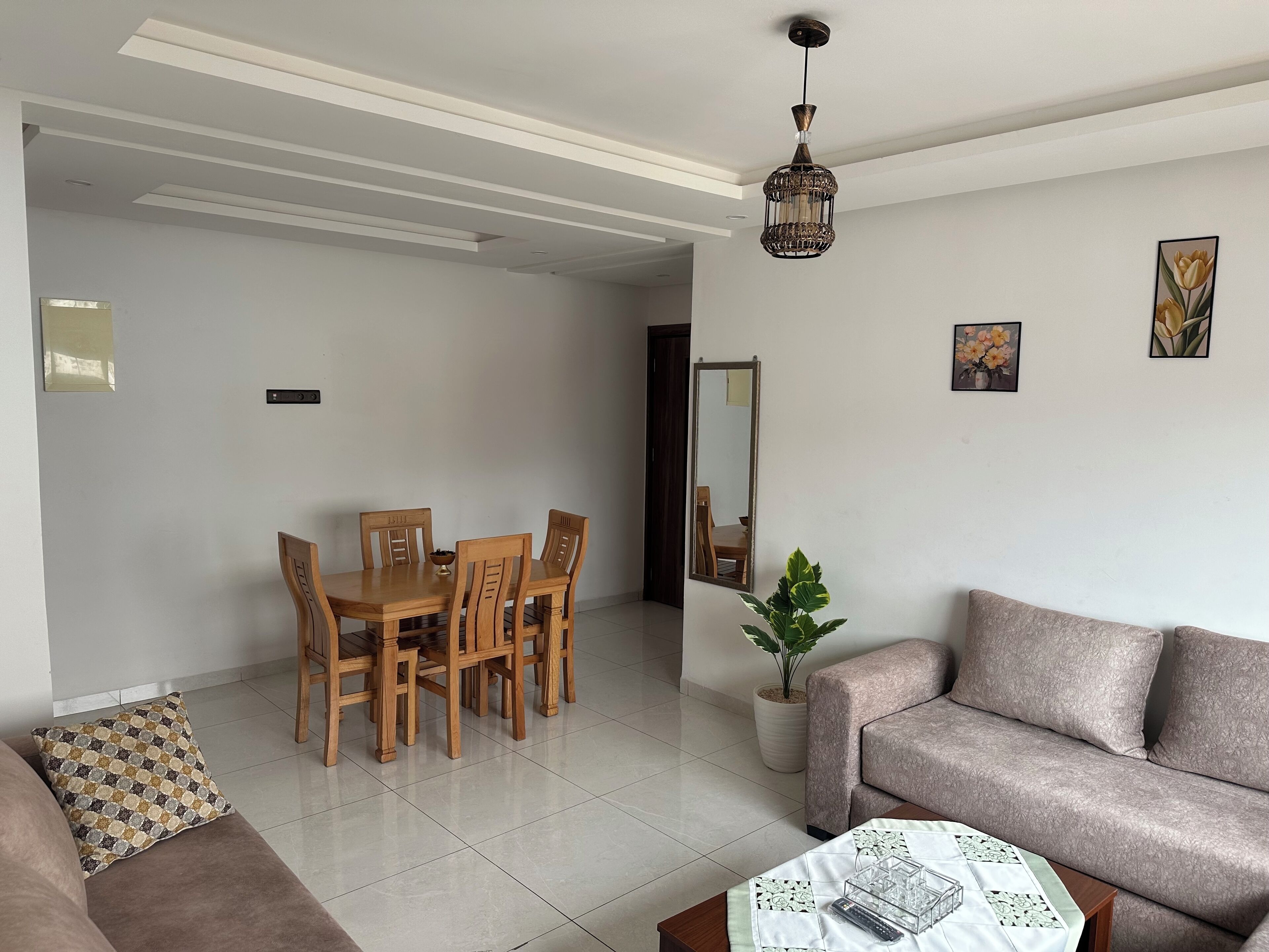 Una sala de estar con comedor, un sofá, una mesa de centro, una planta en maceta y una lámpara colgante.