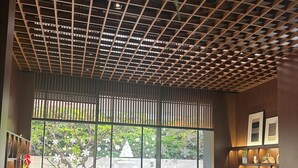 Een modern restaurantinterieur met een plafond in ruitmotief, grote ramen met uitzicht op groen, en een combinatie van zitplaatsen, waaronder tafels en een bank.