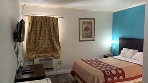 Habitación de hotel con cama, escritorio, televisor, ventana con cortinas y un cuadro en la pared.