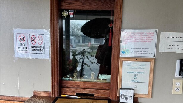 Una recepción con estructura de madera, ventanal de vidrio y varios letreros, incluyendo prohibido fumar y no se admiten mascotas.