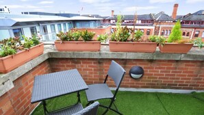 A rooftop patio with a table and chairs, surrounded by potted plants and a brick wall.