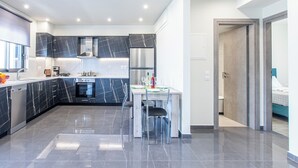 A modern kitchen with dark marble countertops, stainless steel appliances, and a dining area with a glass table. - Mariam Luxury Apts B2 (Chania)