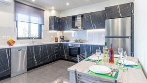 A modern kitchen with black marble cabinets, a stainless steel dishwasher, and a built-in oven. - Mariam Luxury Apts B2 (Chania)