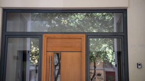 A modern building entrance with a large glass door, a wooden door, and the number 75 above it. - Wonderful central apartment with private parking space. (Larisa)