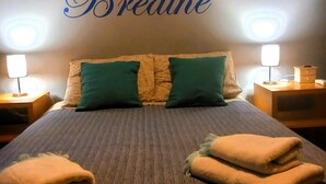 Un letto rifatto con due cuscini, una parete con il testo 'Relax Breathe' e due abat-jour.